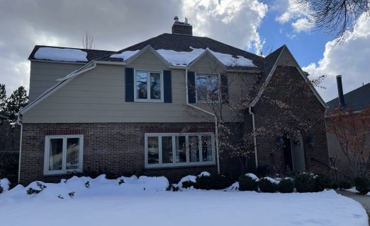 The original facade of a traditional Salt Lake City Avenues home before its exterior remodel, showing the original dark shingle roof, brick lower story, and beige siding upper story.